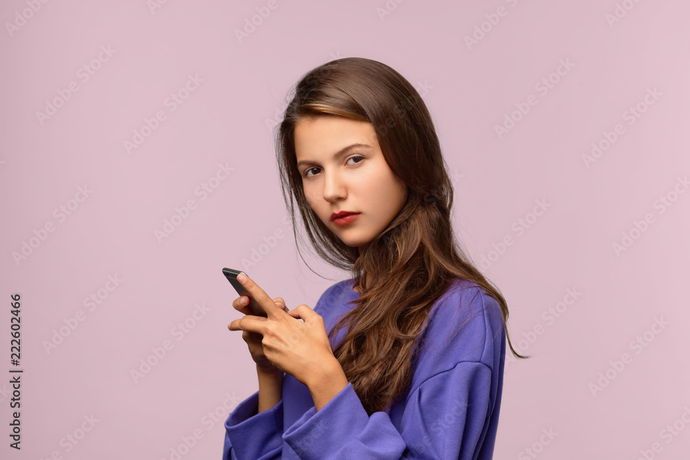 Serious beautiful girl holding the phone with both hands and looking at the camera. Long dark hair, expressive eyes and neutral emotions. Portrait on isolated background in Studio Serious beautiful girl holding the phone with both hands and looking at the camera. Long dark hair, expressive eyes and neutral emotions. Portrait on isolated background in Studio