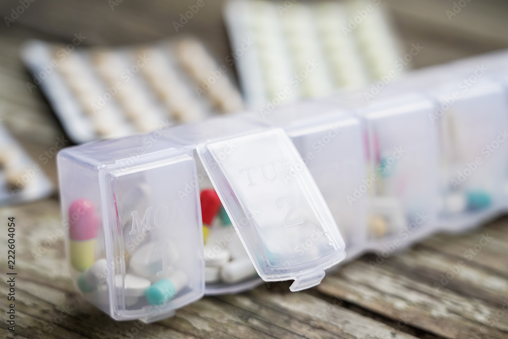 Variety of pills in white plastic pill organizer on weathered wood, free space for text