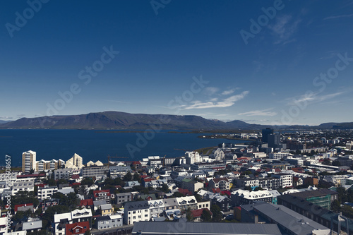 Aerial view on capital of Iceland - city of Reykjavik - ocean bay, hills, mountains, green medows, roadways, hills, streets, houses, traffic, roofing - on sunny day. © Studio Dagdagaz
