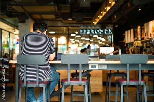 Portrait of unidentified man sitting on the high chair and working with his laptop at the coffee shop