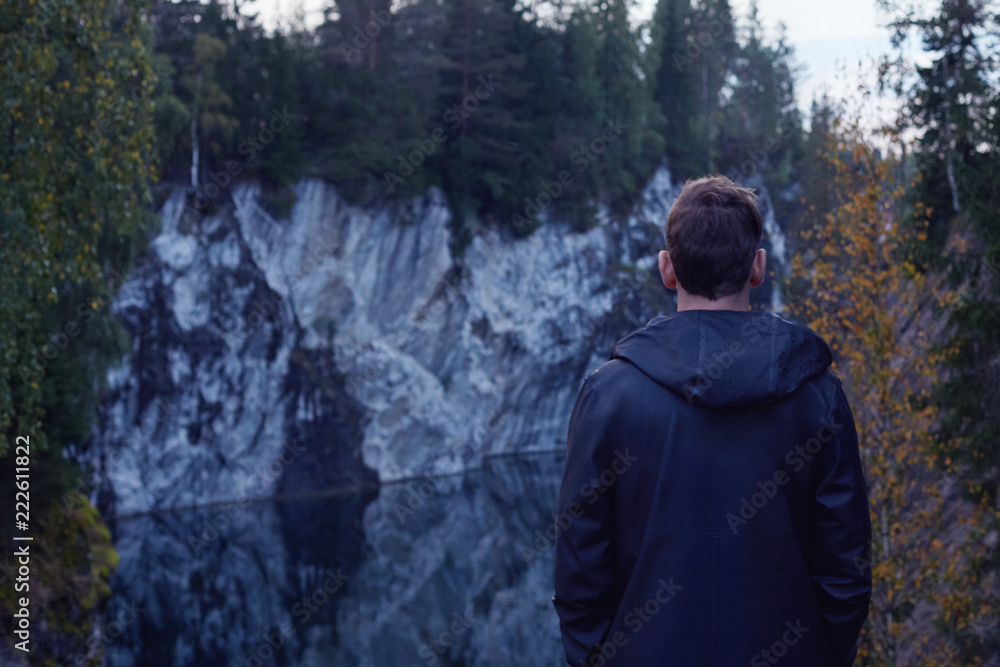 Rear back shot of dark haired man with contemplating nature beauties around him, while standing on sightseeing platform high in mountains of deep forest with azure water of canyon with reflection. Rear back shot of dark haired man with contemplating nature beauties around him, while standing on sightseeing platform high in mountains of deep forest with azure water of canyon with reflection.