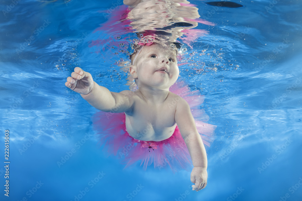 Little girl in a pink dress swims underwater in the pool