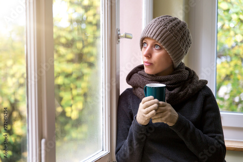 Frau steht an einem Fenster und trinkt ein heißes Getränk, Winter und aufwärmen photo