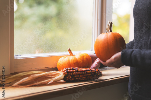 Frau dekoriert auf einer Fensterbank mit Kürbissen und Mais, Herbstdekoration photo