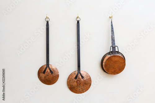 Copper pots and kitchen utinsils hanging on a white painted wall