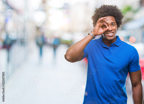Afro american man over isolated background doing ok gesture with hand smiling, eye looking through fingers with happy face. © Krakenimages.com
