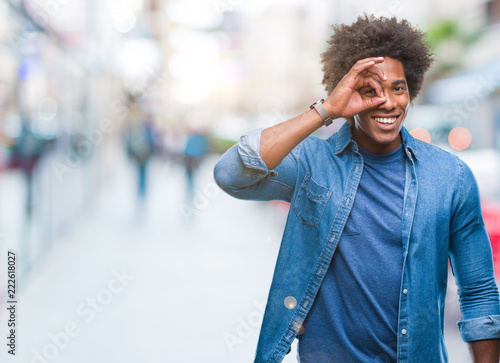 Afro american man over isolated background doing ok gesture with hand smiling, eye looking through fingers with happy face.