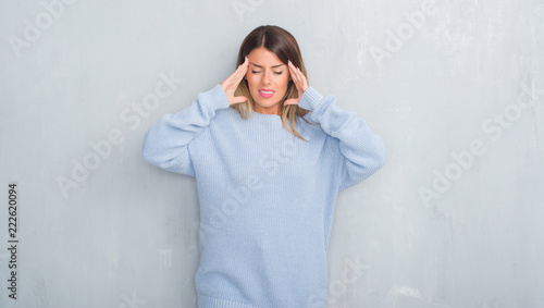 Young adult woman over grey grunge wall wearing winter outfit with hand on head for pain in head because stress. Suffering migraine.