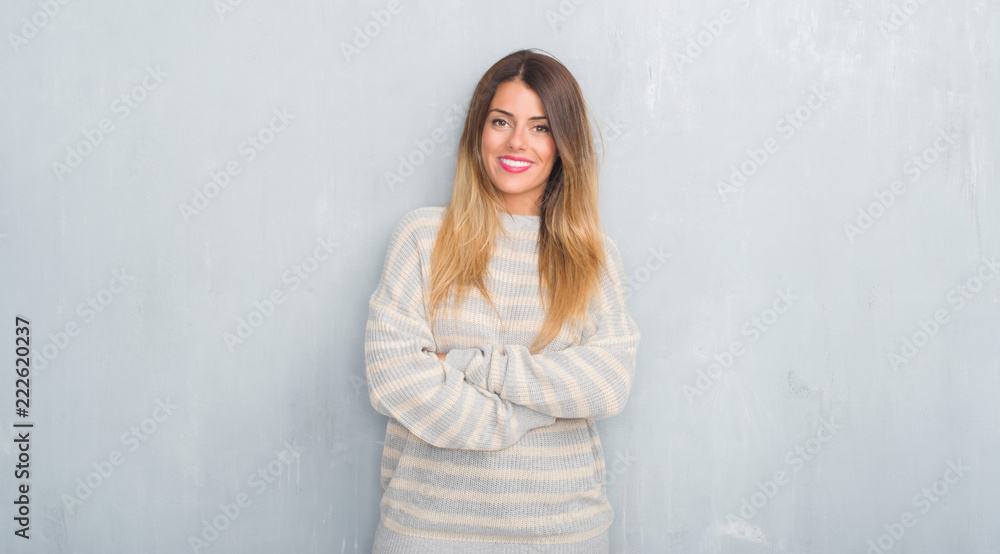 Young adult woman over grunge grey wall wearing winter sweater happy face smiling with crossed arms looking at the camera. Positive person. Young adult woman over grunge grey wall wearing winter sweater happy face smiling with crossed arms looking at the camera. Positive person.