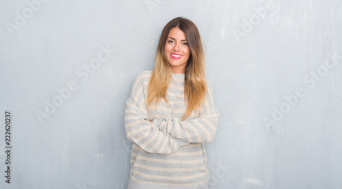 Young adult woman over grunge grey wall wearing winter sweater happy face smiling with crossed arms looking at the camera. Positive person.