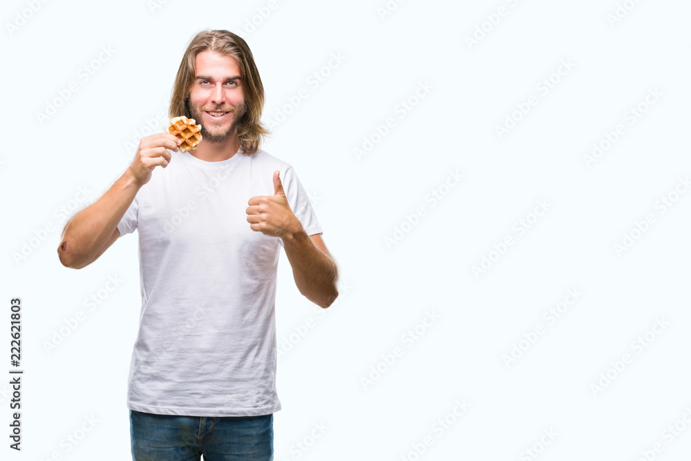 Young handsome man with long hair over isolated background eating waffle happy with big smile doing ok sign, thumb up with fingers, excellent sign Young handsome man with long hair over isolated background eating waffle happy with big smile doing ok sign, thumb up with fingers, excellent sign