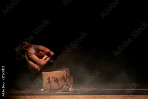 bloody hand holding and opening a box on wooden table in horror and mysterious concept photo