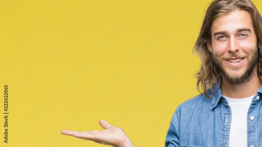 Young handsome man with long hair over isolated background amazed and smiling to the camera while presenting with hand and pointing with finger. Young handsome man with long hair over isolated background amazed and smiling to the camera while presenting with hand and pointing with finger.