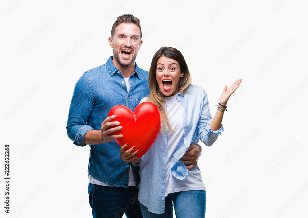 Young couple in love holding red heart over isolated background very happy and excited, winner expression celebrating victory screaming with big smile and raised hands Young couple in love holding red heart over isolated background very happy and excited, winner expression celebrating victory screaming with big smile and raised hands