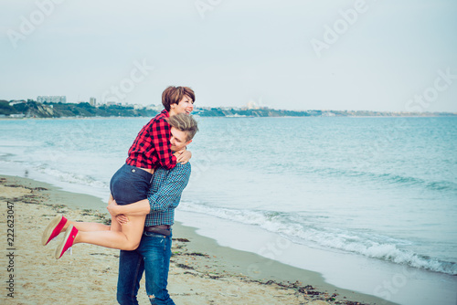 Happy young man carrying his woman on the beach. Couple enjoying a day, having fun. Boyfriend and girlfriend having date. Concept of lovers happy moments on holiday. Selective focus, copy space.