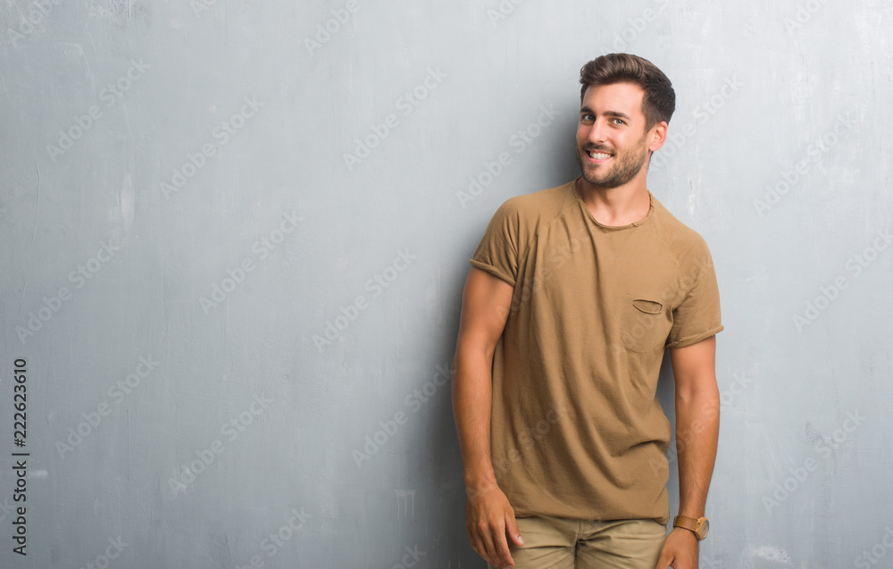 Handsome young man over grey grunge wall looking away to side with smile on face, natural expression. Laughing confident. Handsome young man over grey grunge wall looking away to side with smile on face, natural expression. Laughing confident.