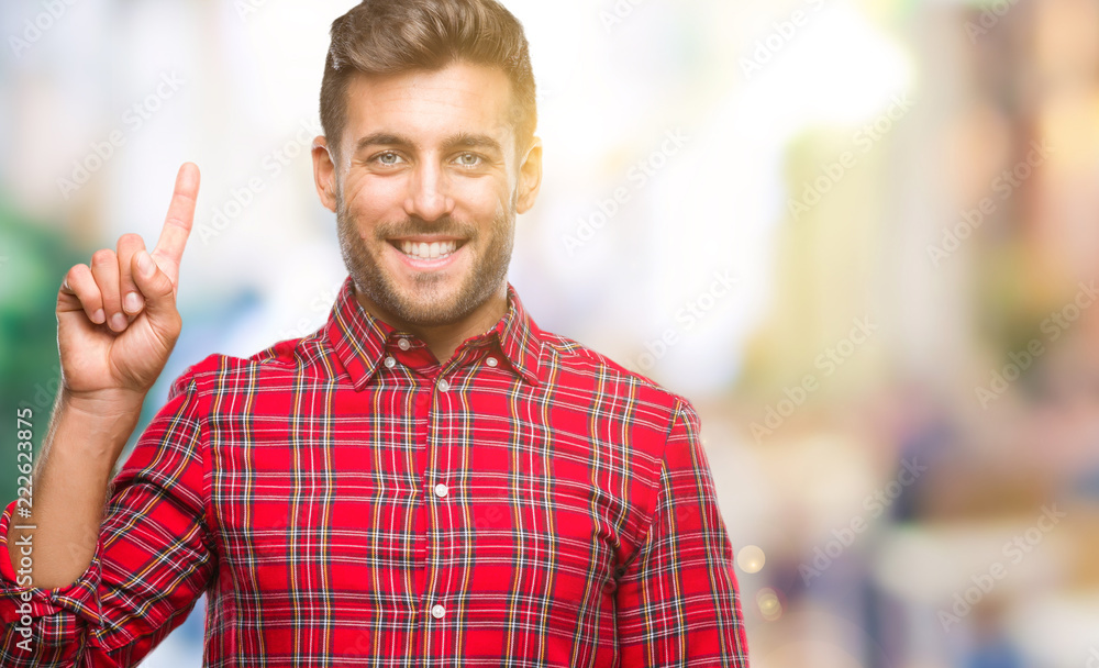 Obraz premium Young handsome man over isolated background showing and pointing up with finger number one while smiling confident and happy.