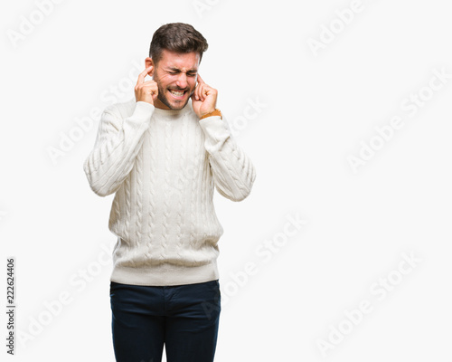 Young handsome man wearing winter sweater over isolated background covering ears with fingers with annoyed expression for the noise of loud music. Deaf concept.