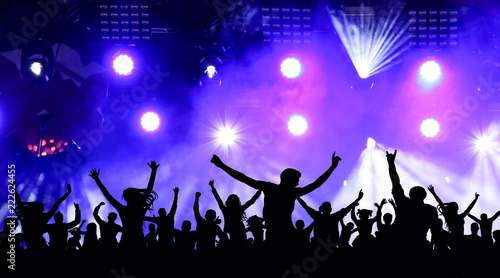 Dancing youth party, illustration. Crowd of cheerful people at a concert. Silhouettes of a crowd of fans in front of bright scene lights