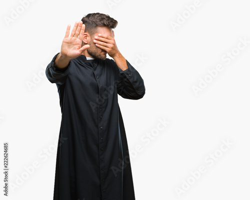 Young catholic christian priest man over isolated background covering eyes with hands and doing stop gesture with sad and fear expression. Embarrassed and negative concept.