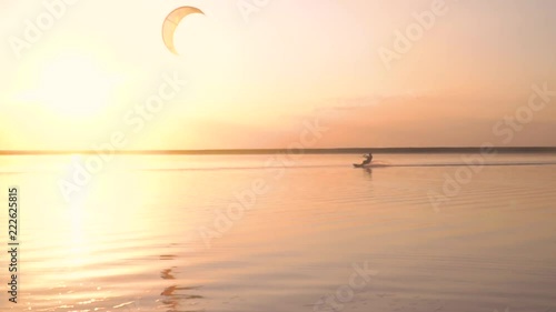 A man in the rays of dawn is engaged in kitesurfing on the lake and make somersalut in the air