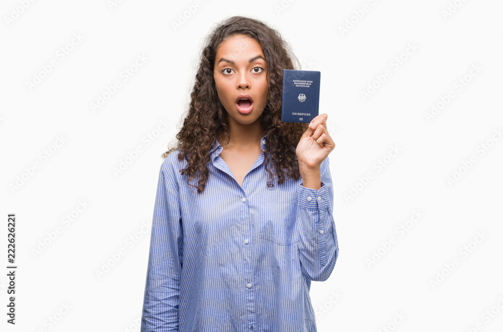 Young hispanic woman holding passport of Germany scared in shock with a surprise face, afraid and excited with fear expression Young hispanic woman holding passport of Germany scared in shock with a surprise face, afraid and excited with fear expression