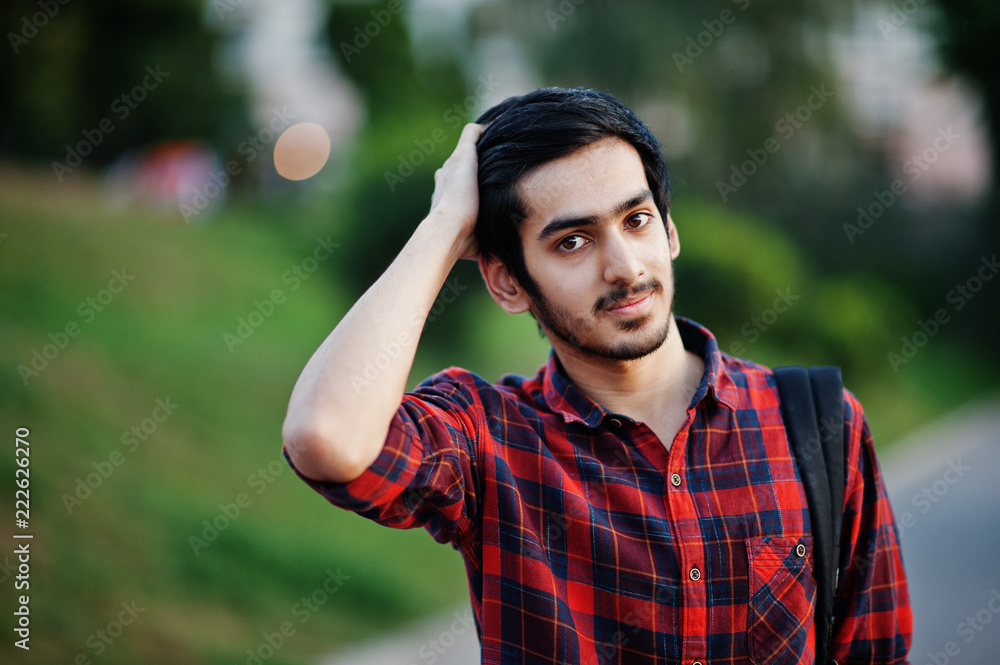 Young indian student man at red checkered shirt and jeans with backpack posed at street. Young indian student man at red checkered shirt and jeans with backpack posed at street.