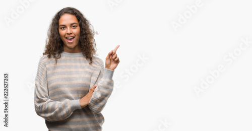 Beautiful young hispanic woman wearing stripes sweater with a big smile on face, pointing with hand and finger to the side looking at the camera. © Krakenimages.com