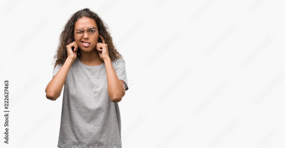 Beautiful young hispanic woman wearing glasses covering ears with fingers with annoyed expression for the noise of loud music. Deaf concept.