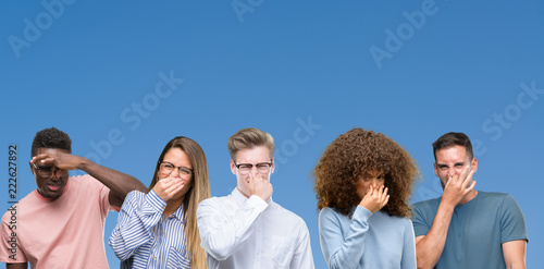 Foto Composition of group of friends over blue blackground smelling something stinky and disgusting, intolerable smell, holding breath with fingers on nose