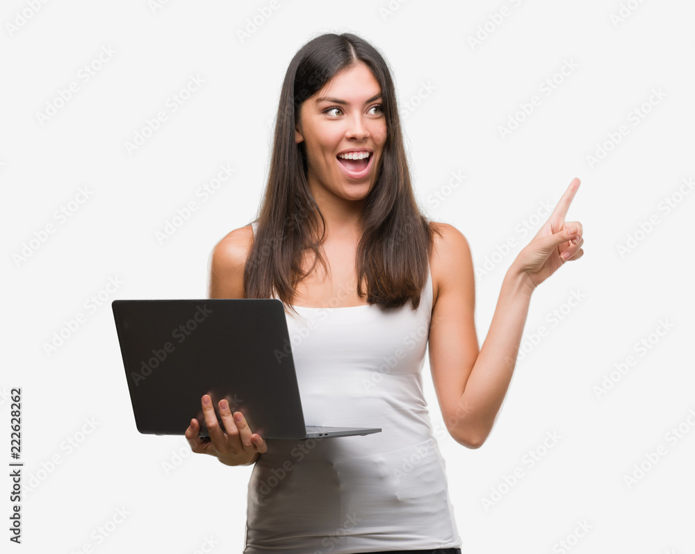 Young hispanic woman using computer laptop very happy pointing with hand and finger to the side Young hispanic woman using computer laptop very happy pointing with hand and finger to the side