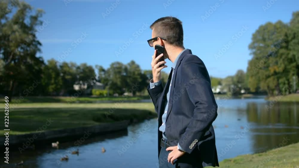 Young businessman in a suit and sunglasses is using mobile phone smartphone talking in front of a beautiful landscape Young businessman in a suit and sunglasses is using mobile phone smartphone talking in front of a beautiful landscape
