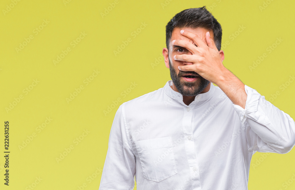 Adult hispanic man over isolated background peeking in shock covering face and eyes with hand, looking through fingers with embarrassed expression. Adult hispanic man over isolated background peeking in shock covering face and eyes with hand, looking through fingers with embarrassed expression.