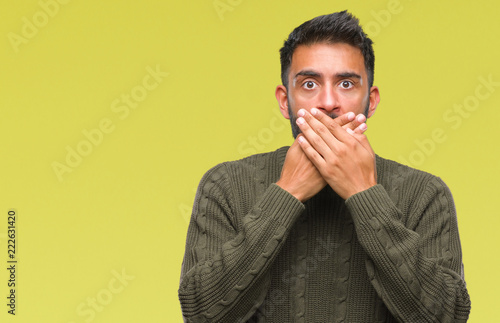 Adult hispanic man wearing winter sweater over isolated background shocked covering mouth with hands for mistake. Secret concept.