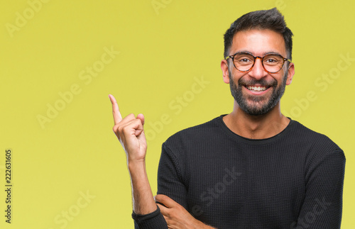 Adult hispanic man wearing glasses over isolated background with a big smile on face, pointing with hand and finger to the side looking at the camera.