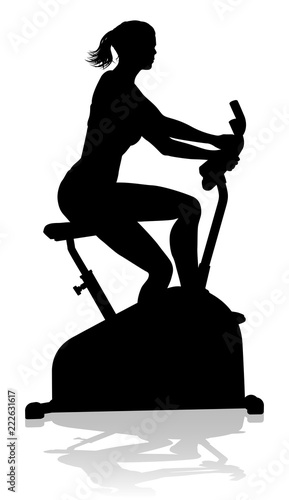 A woman in silhouette using a stationary exercise spin bike piece of gym equipment fitness machine 