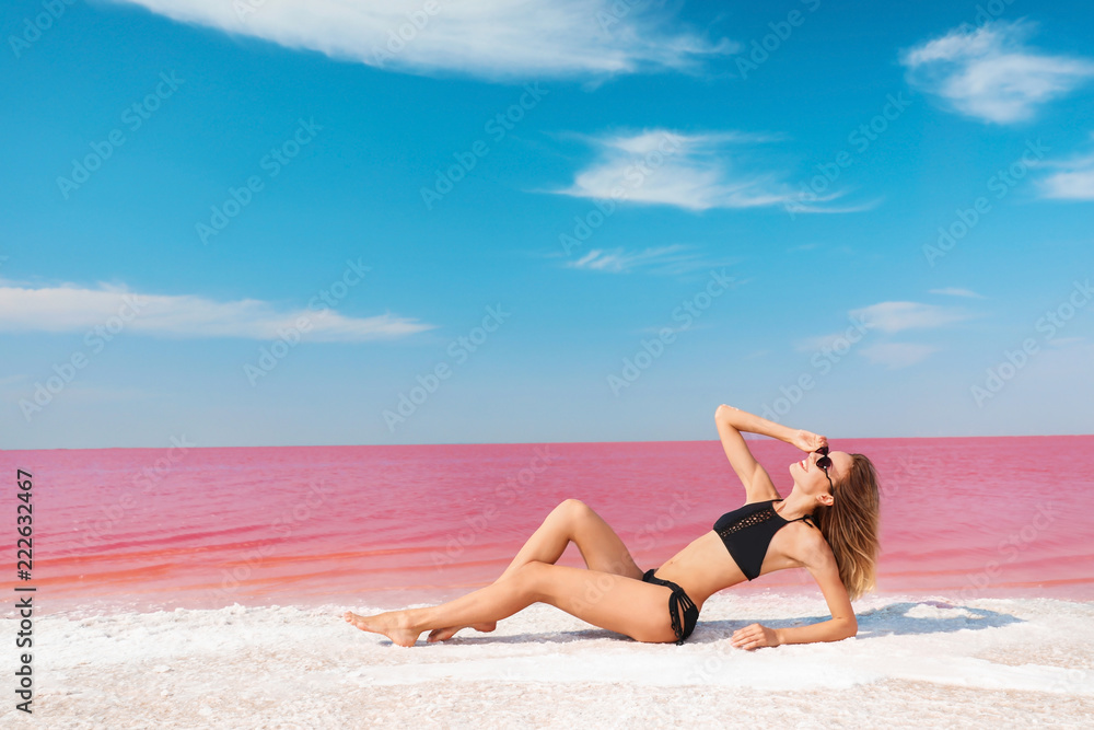 Beautiful woman in swimsuit lying near pink lake on sunny day Beautiful woman in swimsuit lying near pink lake on sunny day