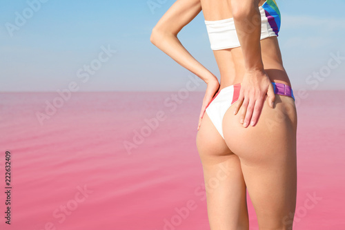 Beautiful woman in swimsuit posing near pink lake on sunny day, closeup