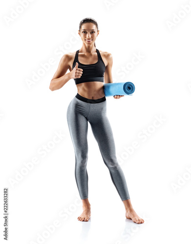 Young sporty girl with yoga mat standing isolated on white background. Concept of healthy life and natural balance between body and mental development. Full length