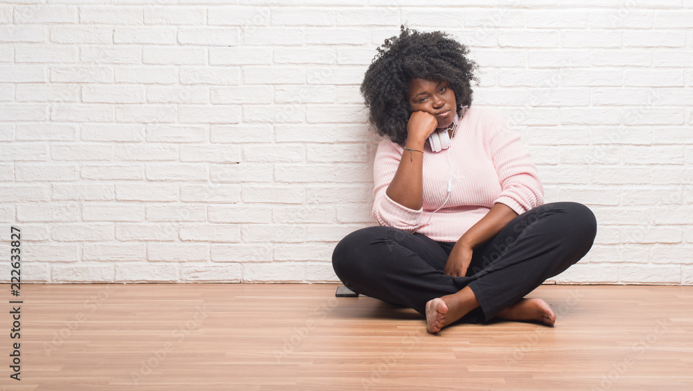 Young african american woman sitting on the floor wearing headphones thinking looking tired and bored with depression problems with crossed arms. Young african american woman sitting on the floor wearing headphones thinking looking tired and bored with depression problems with crossed arms.