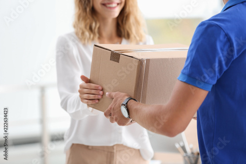 Young woman receiving parcel from courier indoors photo