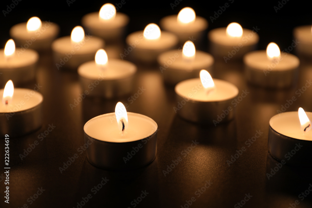 Burning candles on table in darkness, closeup. Funeral symbol