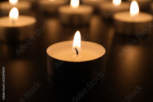 Burning candle on table in darkness, closeup. Funeral symbol