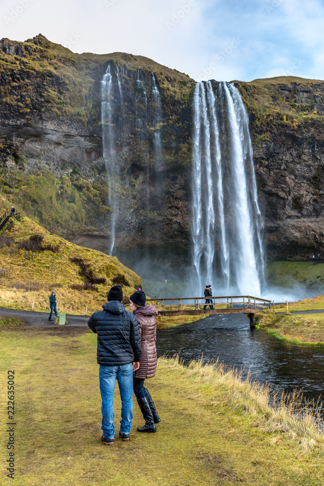 Seljalandsfoss, Iceland - Oct 22th 2017 - Young couple enjoying the Seljalandsfoss fall in a overcast day in Iceland.