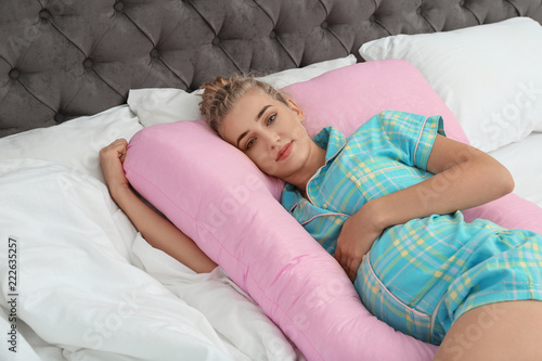 Beautiful pregnant woman lying with maternity pillow on bed at home