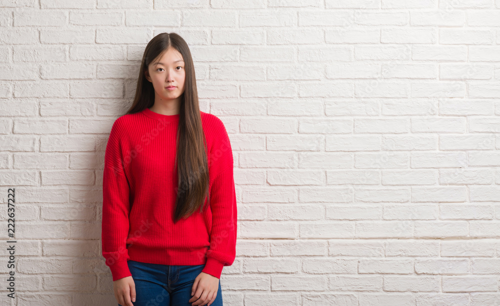 Young Chinese woman over brick wall with serious expression on face. Simple and natural looking at the camera. Young Chinese woman over brick wall with serious expression on face. Simple and natural looking at the camera.