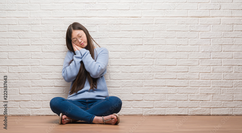 Young Chinese woman sitting on the floor over brick wall sleeping tired dreaming and posing with hands together while smiling with closed eyes. Young Chinese woman sitting on the floor over brick wall sleeping tired dreaming and posing with hands together while smiling with closed eyes.