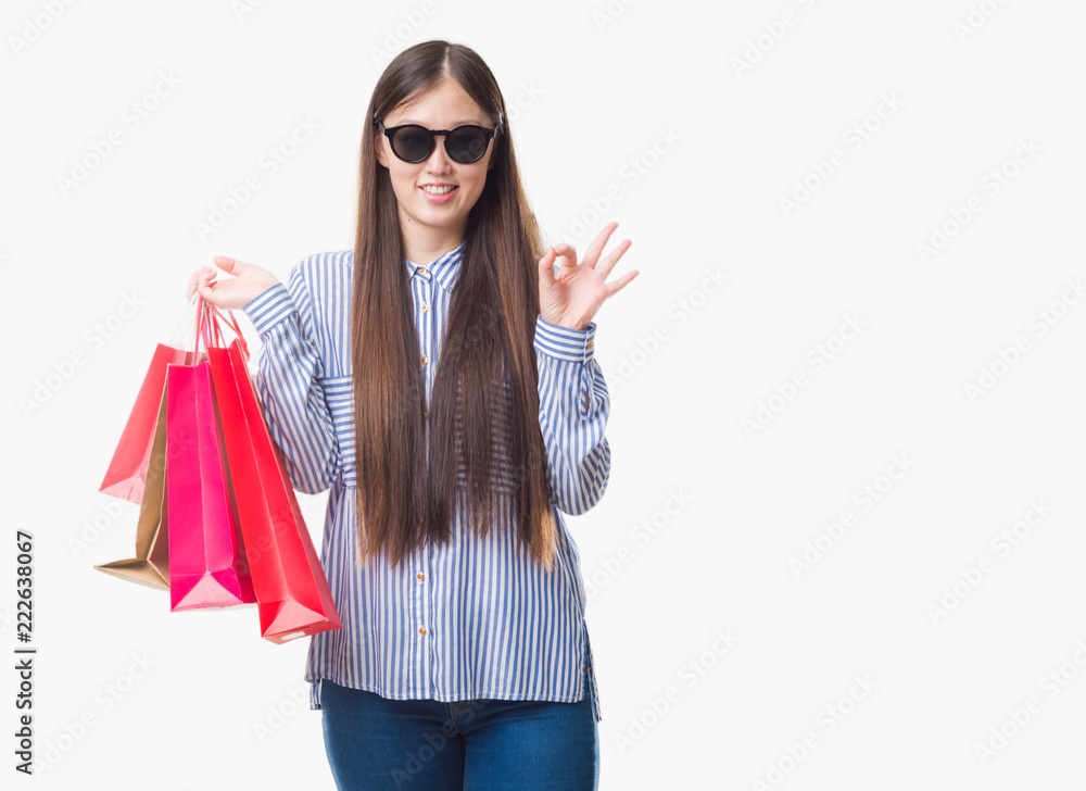 Young Chinese woman over isolated background holding shopping bags on sales doing ok sign with fingers, excellent symbol Young Chinese woman over isolated background holding shopping bags on sales doing ok sign with fingers, excellent symbol