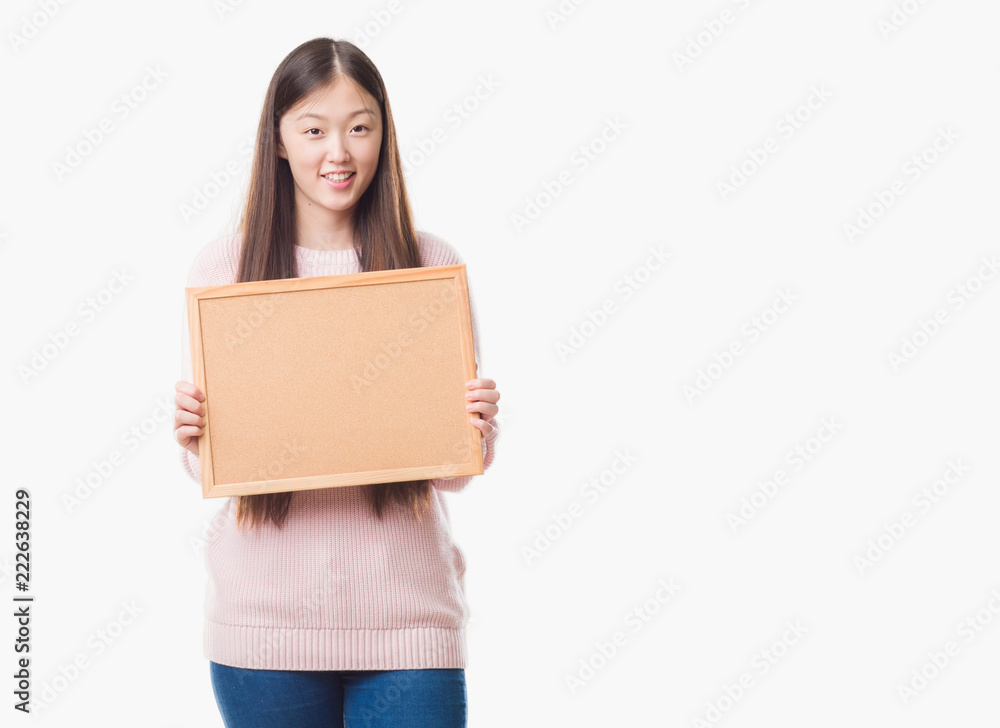 Young Chinese woman over isolated background holding corkboard with a happy face standing and smiling with a confident smile showing teeth Young Chinese woman over isolated background holding corkboard with a happy face standing and smiling with a confident smile showing teeth