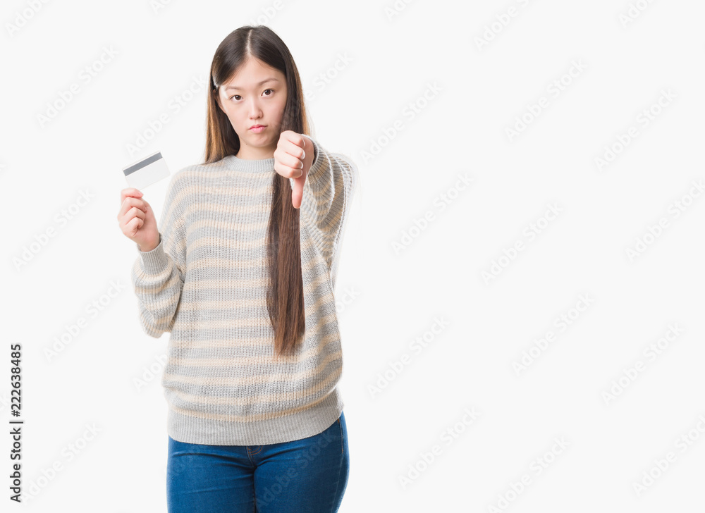 Young Chinese woman over isolated background holding credit card with angry face, negative sign showing dislike with thumbs down, rejection concept Young Chinese woman over isolated background holding credit card with angry face, negative sign showing dislike with thumbs down, rejection concept